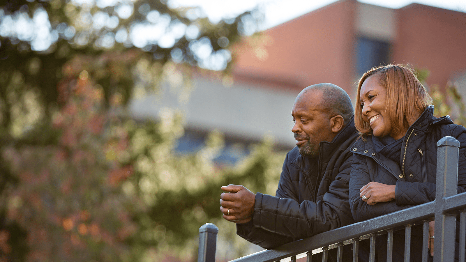 image of a male and female smiling and leaning on a fence