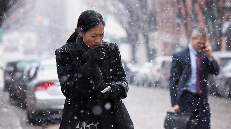 Woman coughing while walking along a snowy city street