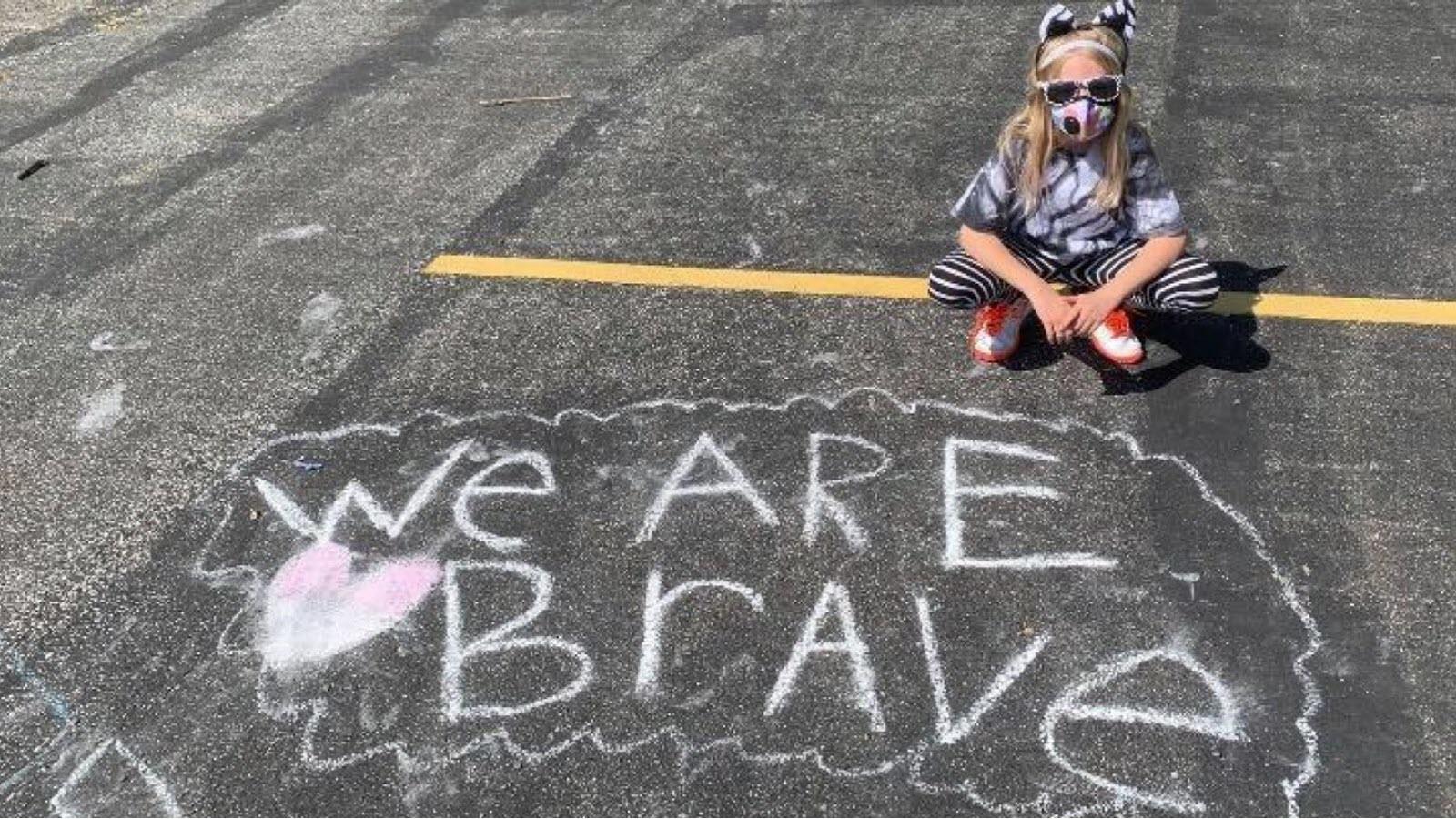 Little girl dressed in zebra attire with a chalk sign that says We Are Brave