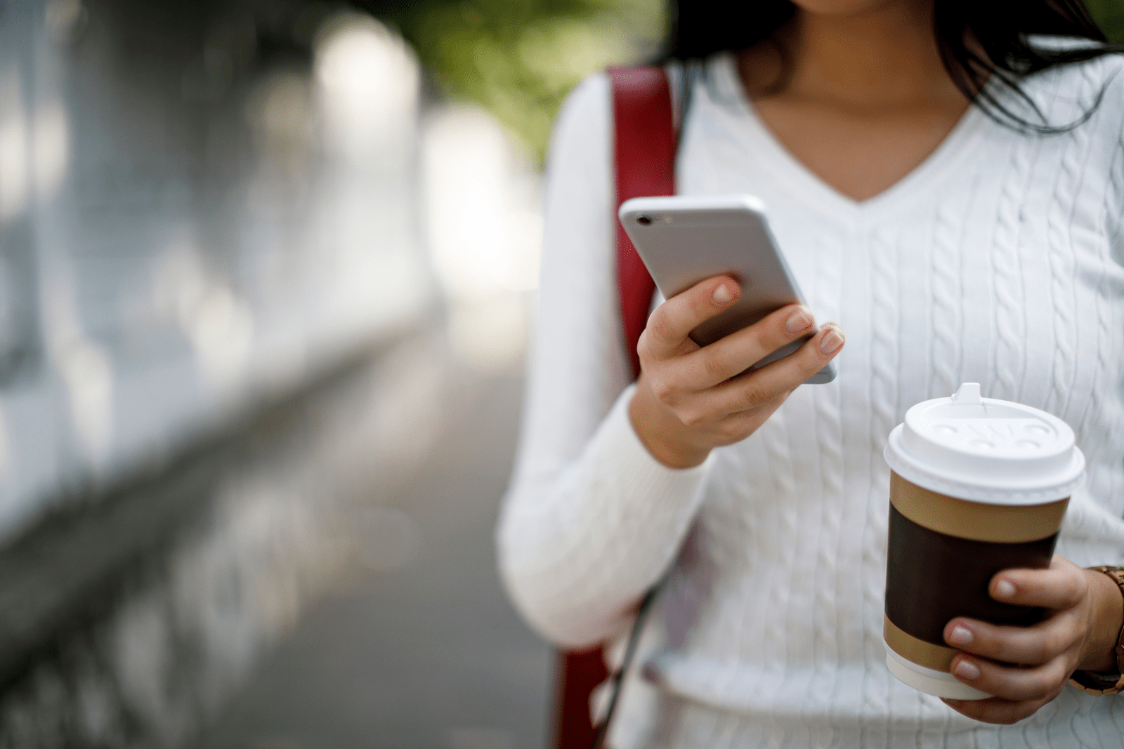 woman walking with a coffee in hand while looking at her mobile phone