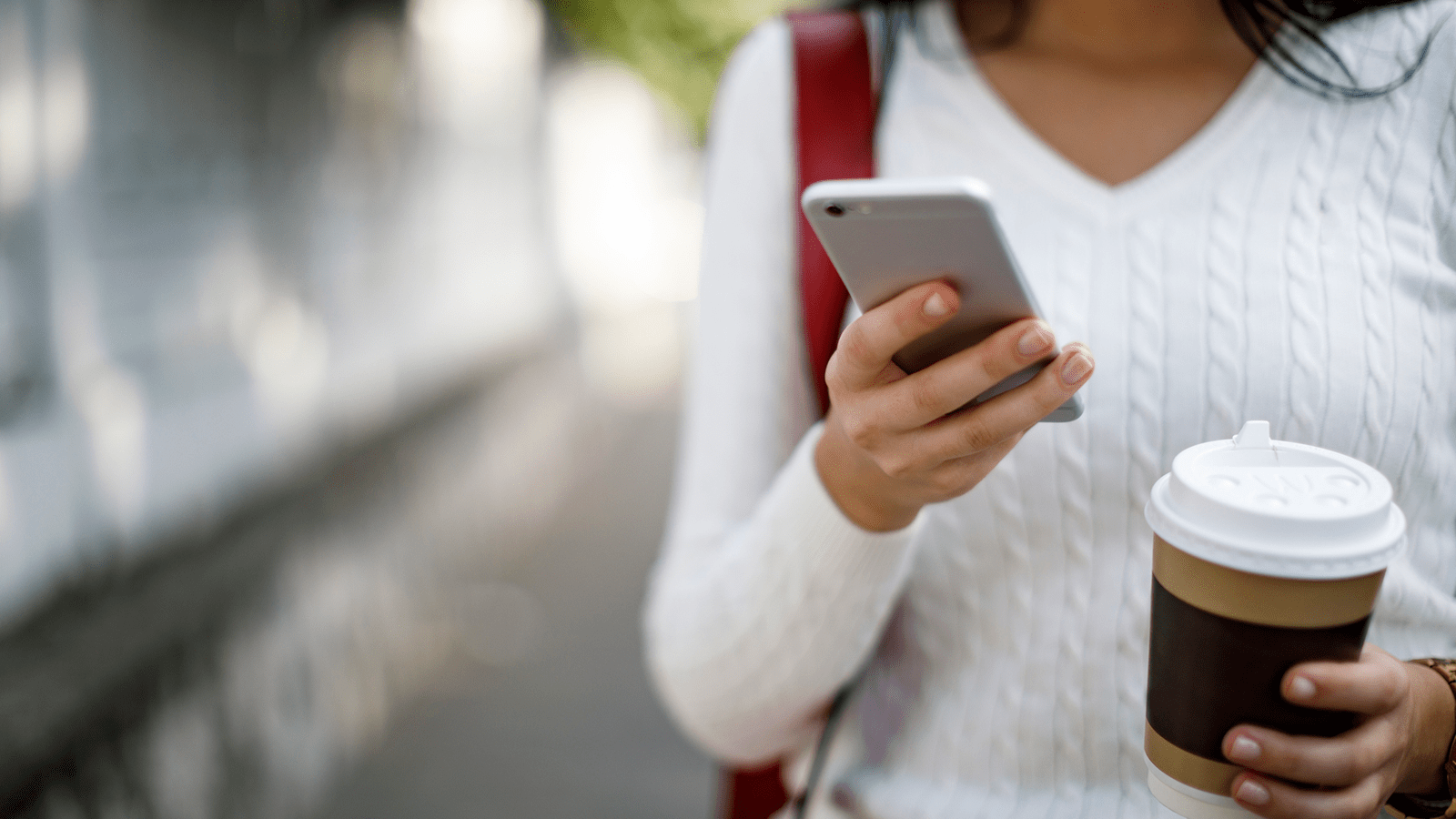 woman walking with a coffee in hand while looking at her mobile phone