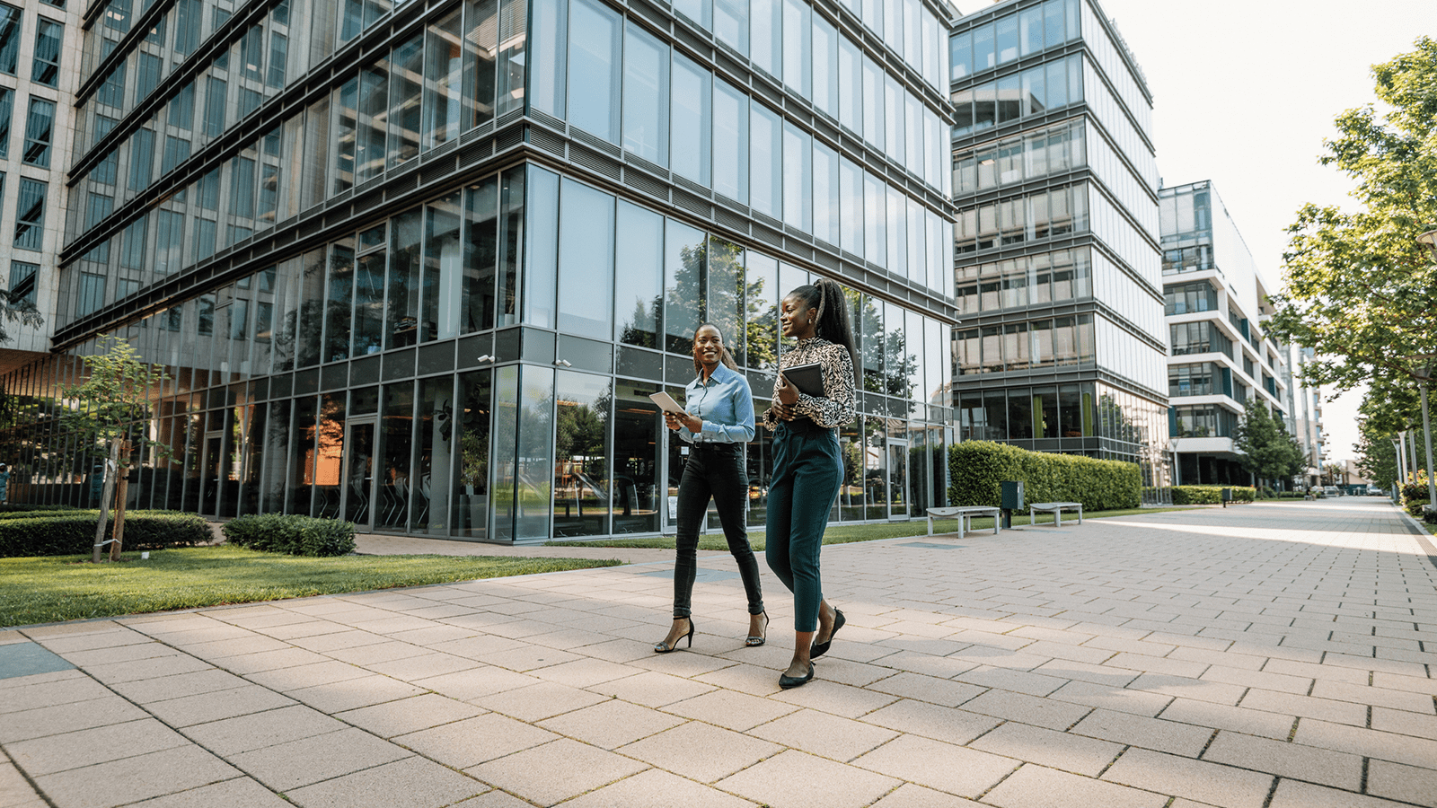 Two women walking outdoors between office buildings