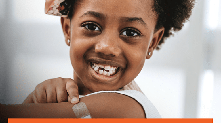 Picture of a young girl who is smiling while pointing to a band aid on her upper arm