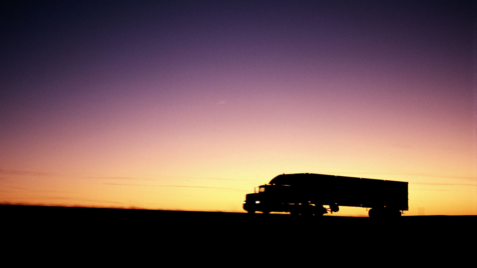 Tractor-trailer on a country road at sunset.