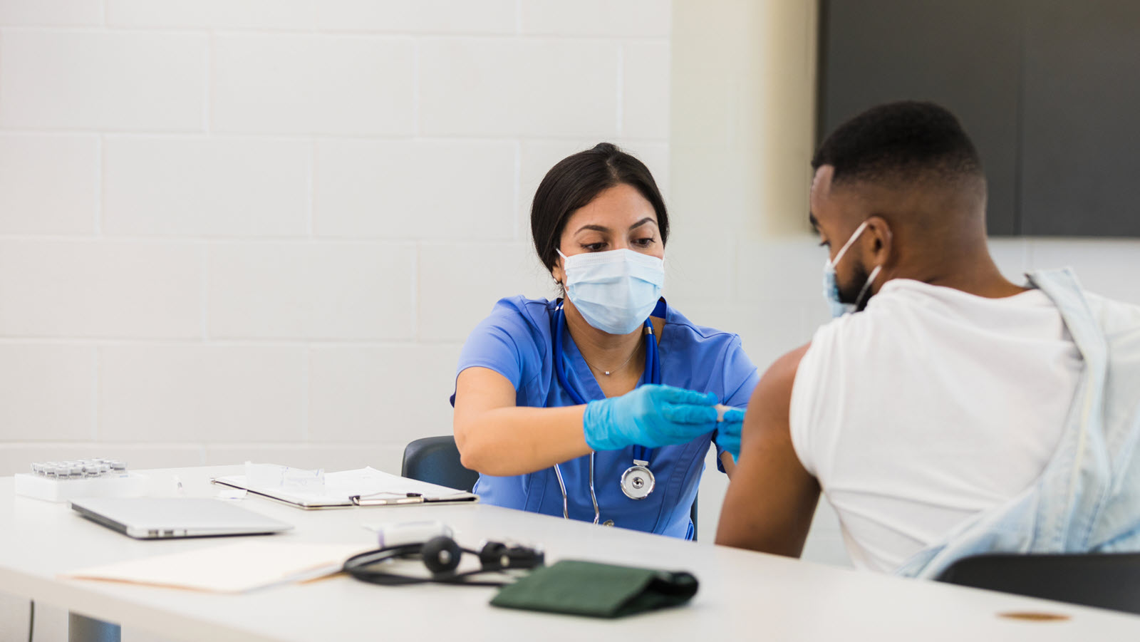 After administering a flu or COVID vaccine, a female nurse places a bandage on a male patient's arm.
