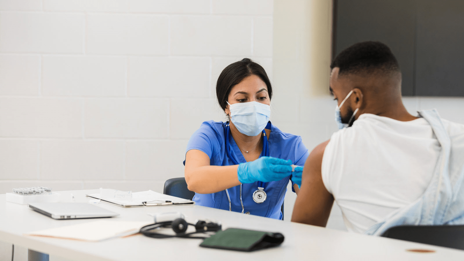 After administering a flu or COVID vaccine, a female nurse places a bandage on a male patient's arm.