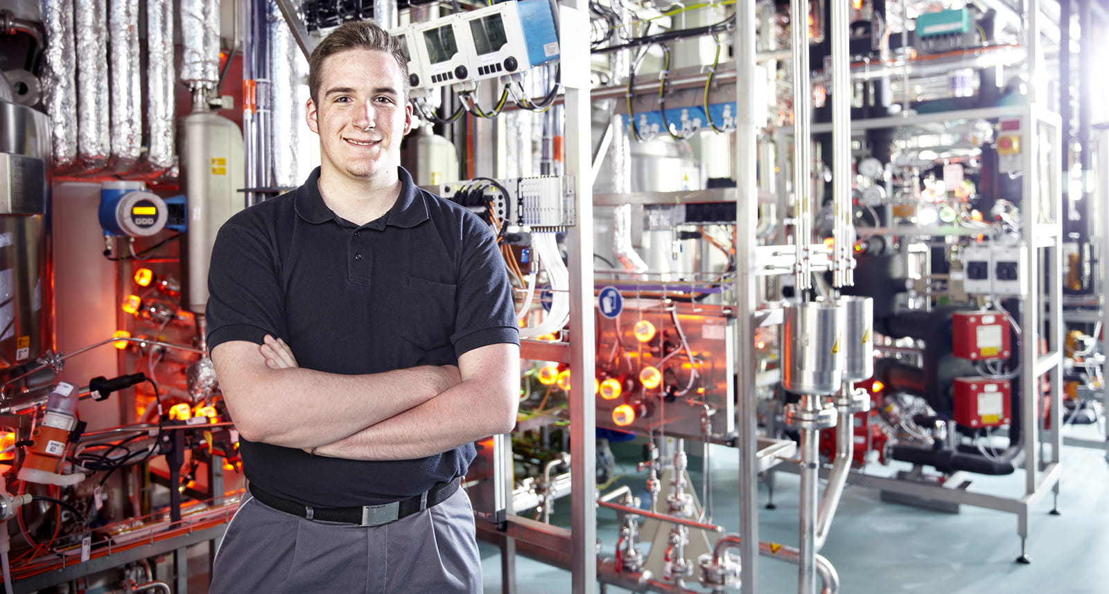  Young man stands in front of machine and smiles.