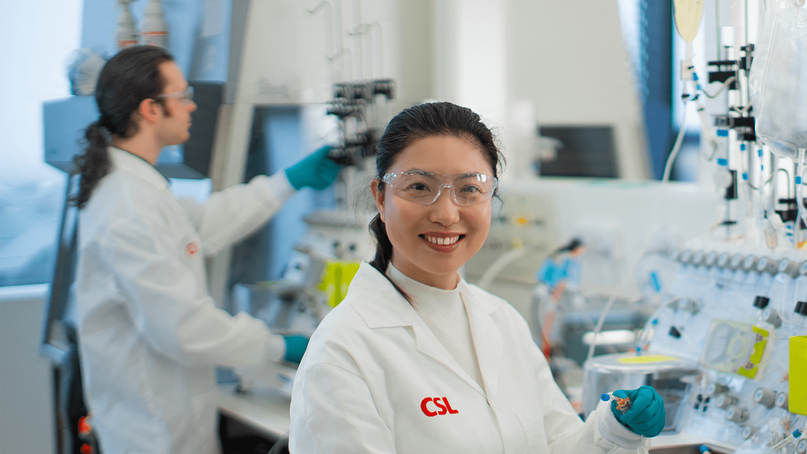 Two scientists in a laboratory wearing turquoise gowns.