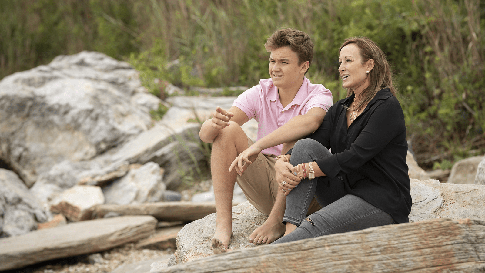 Photo of a mother and son talking while sitting outside on a rock 