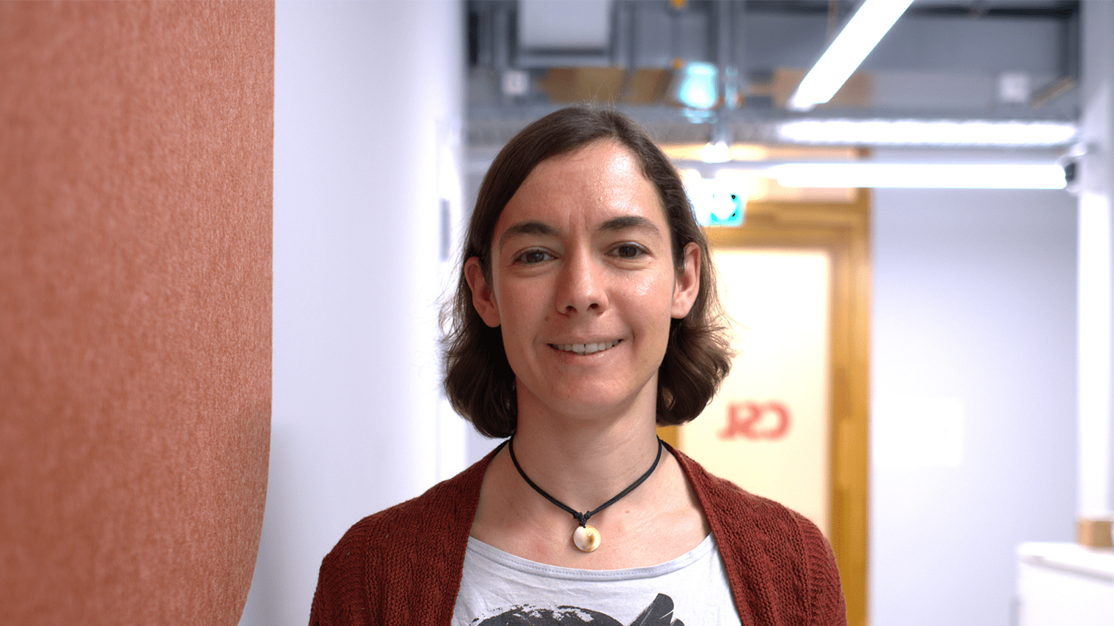 Photograph of lady in casual clothes smiling in an office environment.