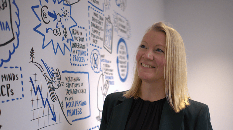 Photo of smiling woman standing in front of a wall covered in STEM-themed art
