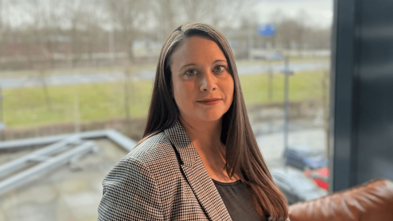 Photograph of lady in an office standing next to a window smiling at the camera.