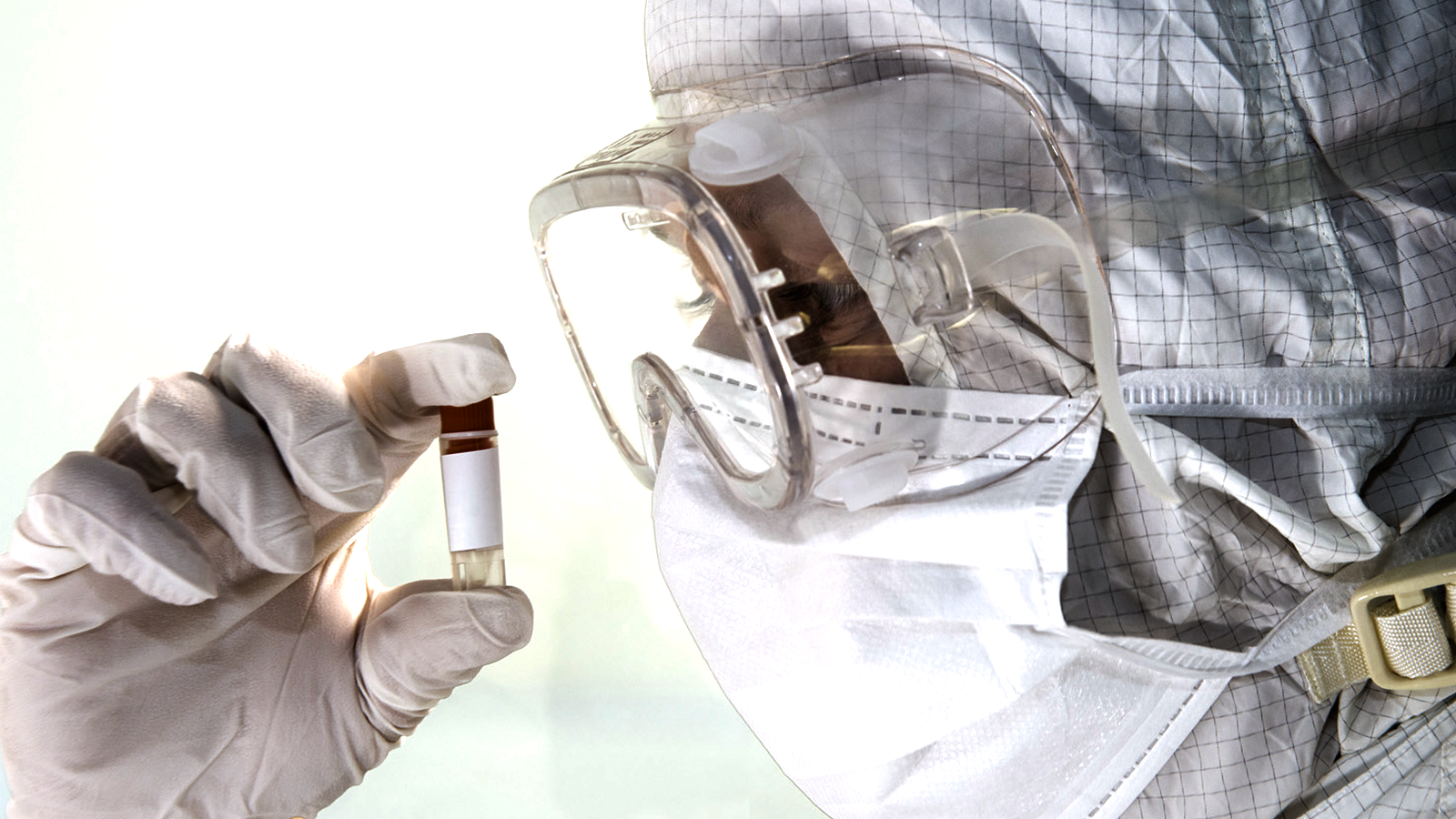 gowned scientist looking closely at a vial