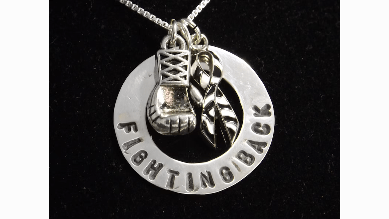 Silver necklace charm of a boxing glove and zebra ribbon that says Fighting Back