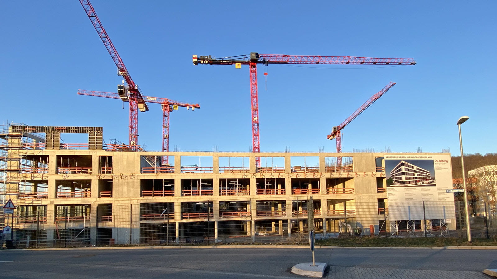 Several red construction cranes at work on upper floors of a new research building in Marburg, Germany