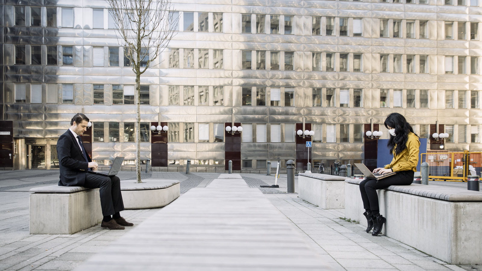 People in an outdoor square - one is masked the other is not