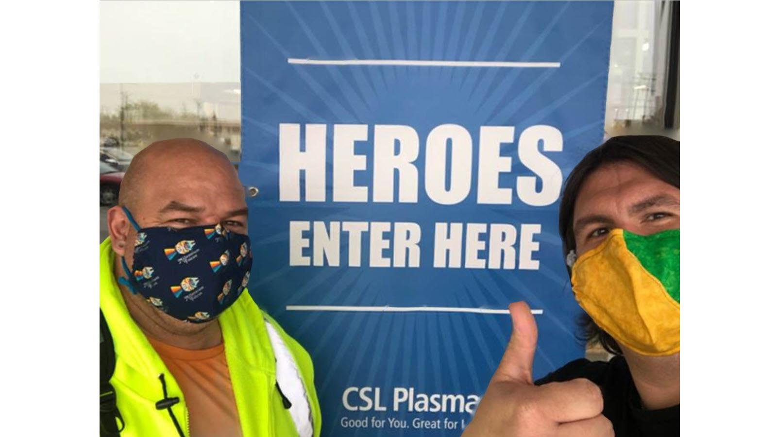Two CSL Behring employees - Jason Tanner and Guy Redman - outside a CSL Plasma Center showing thumbs up