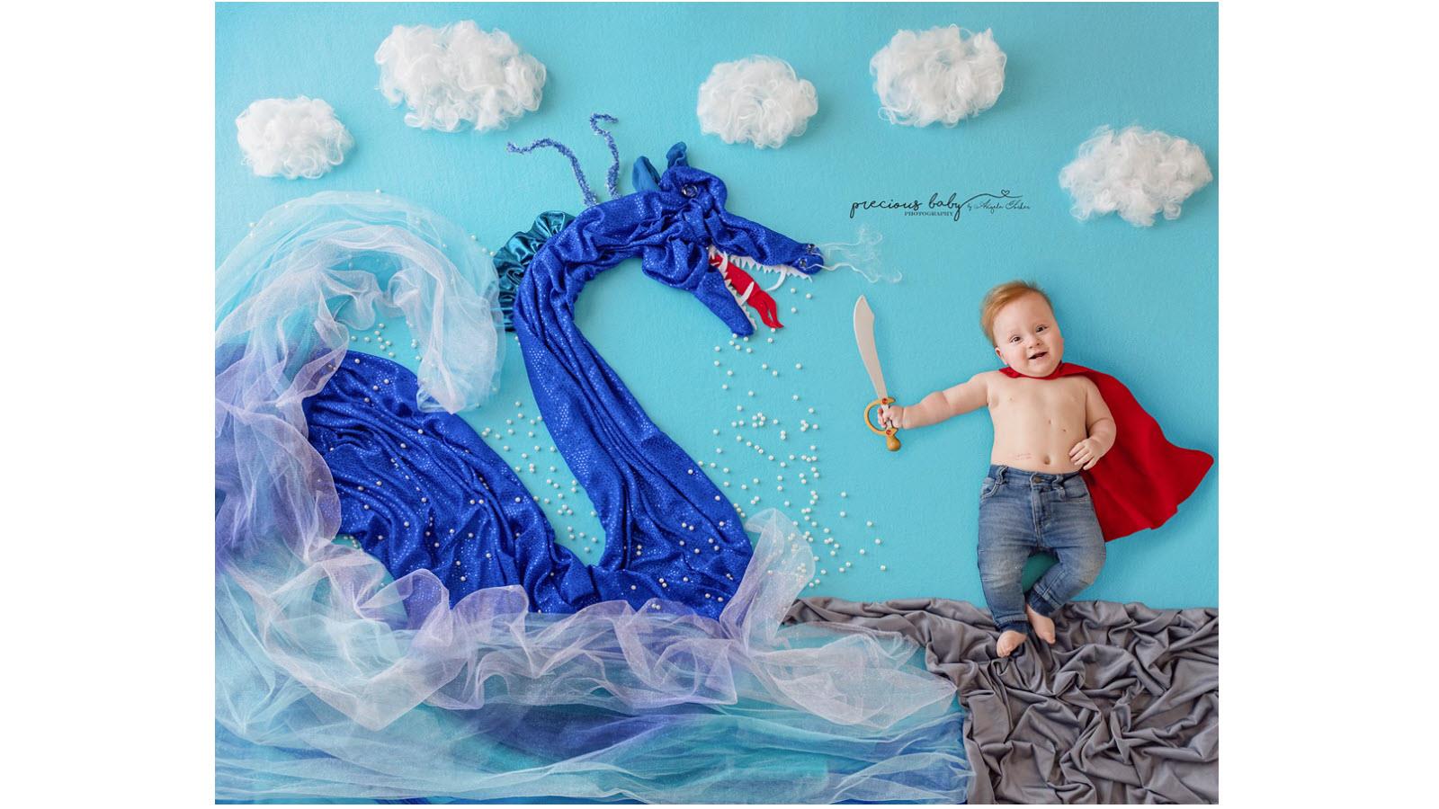 Baby wearing a cape and holding a sword alongside a blue dragon