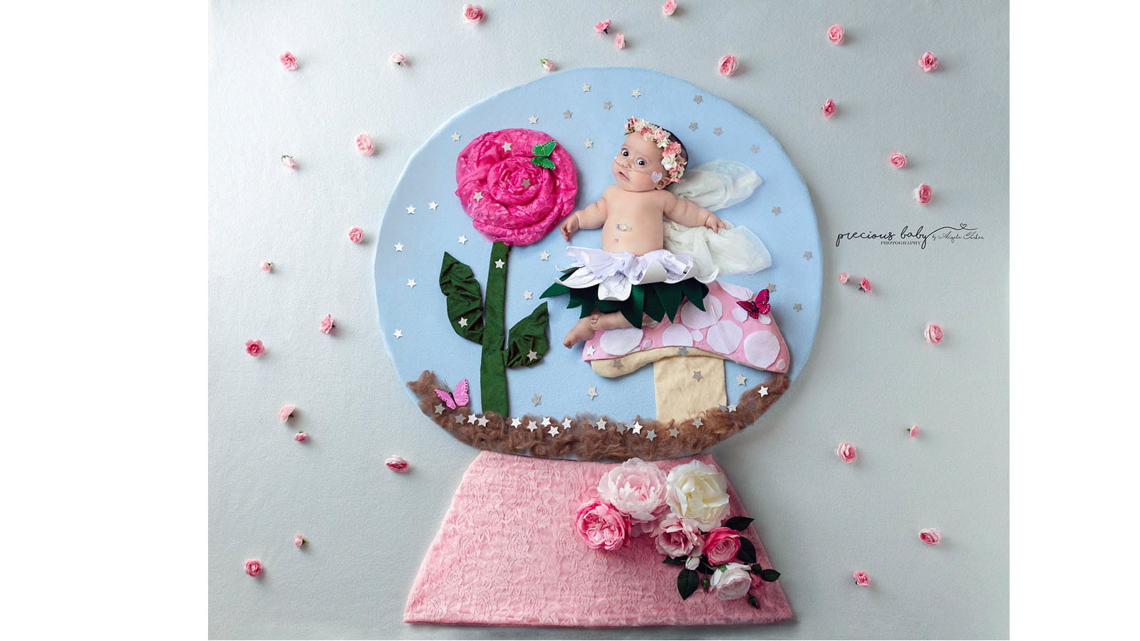 Baby dressed as a fairy wears a floral crown inside a snow globe scene