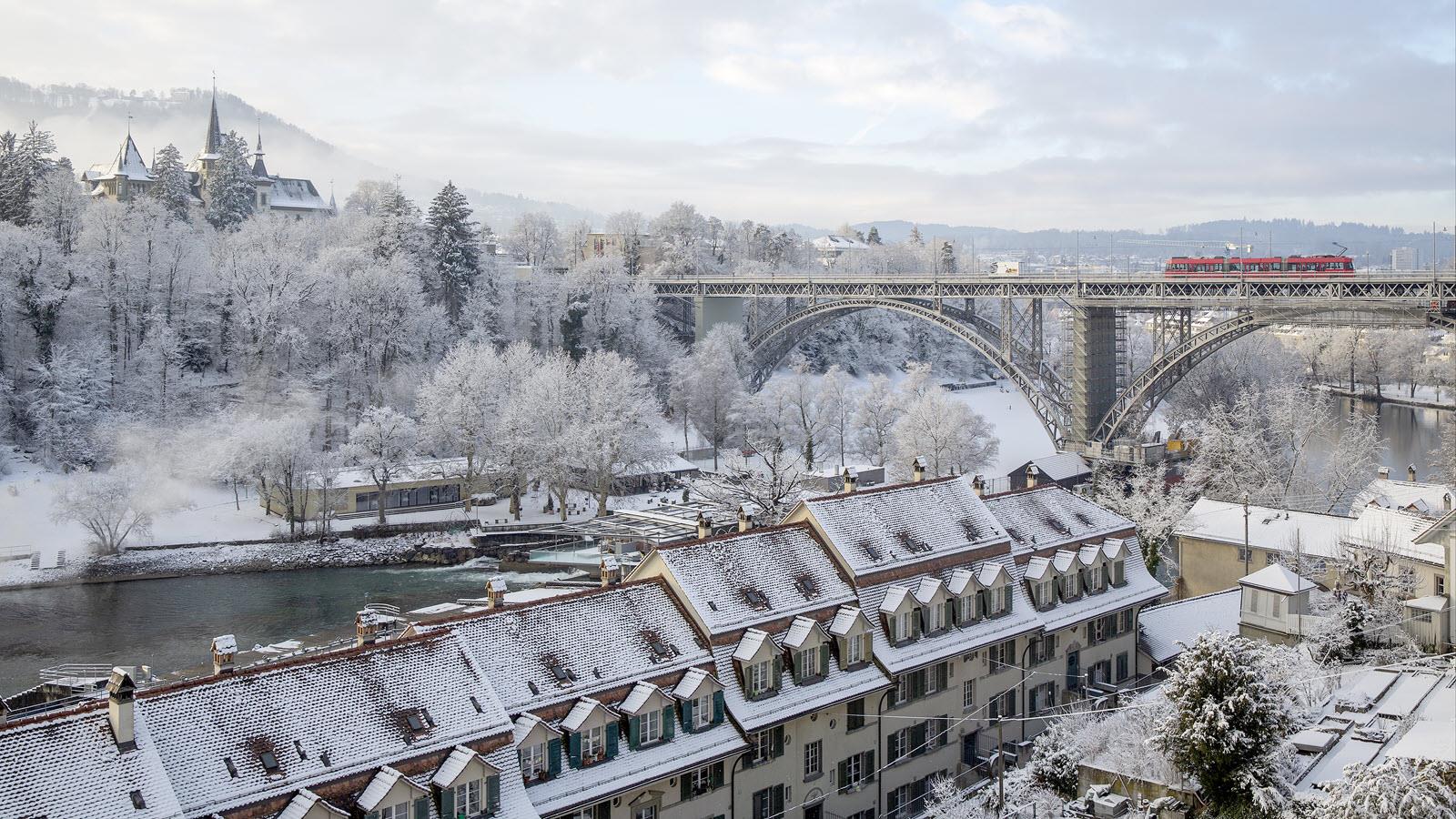 Red train crosses the elevated tracks above the Aare River in Bern, Switzerland.