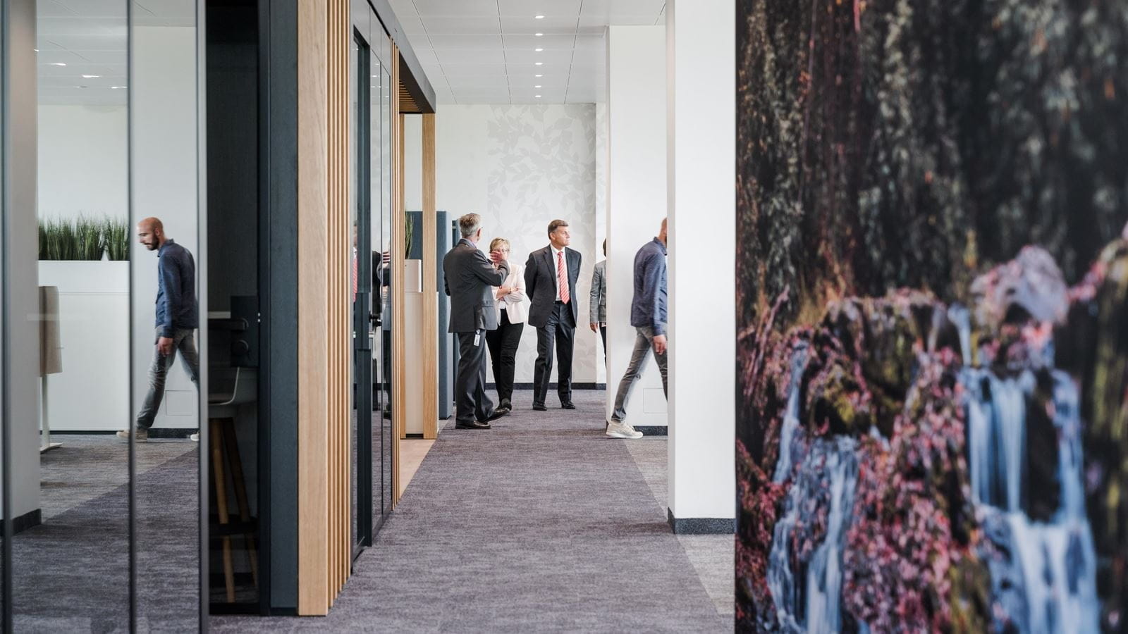 A group tours the M600 R&D building. A waterfall photograph covers the wall.