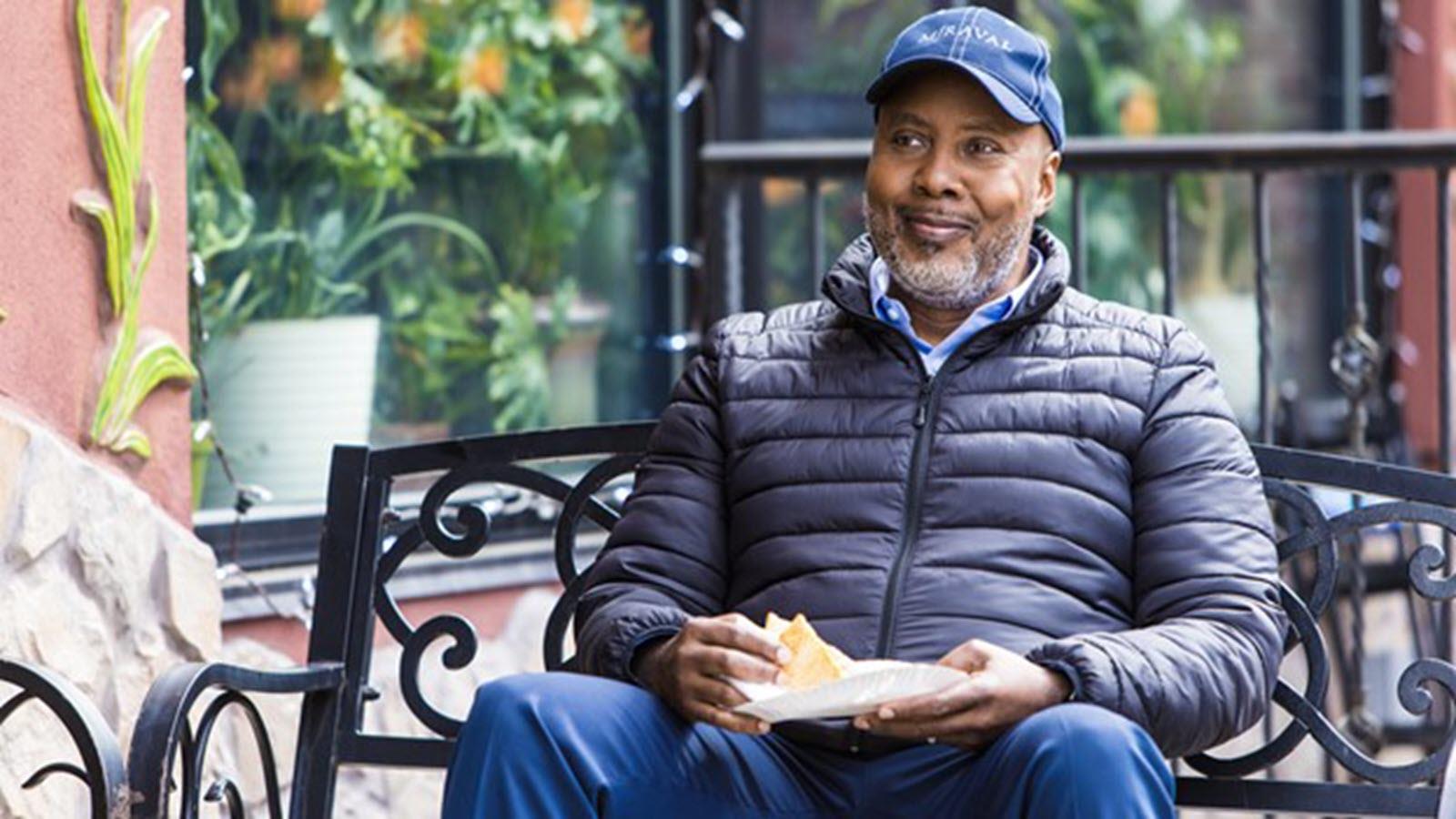 Photo of Arthur, a CIDP patient, sitting outside in a ball cap holding a slice of pizza.