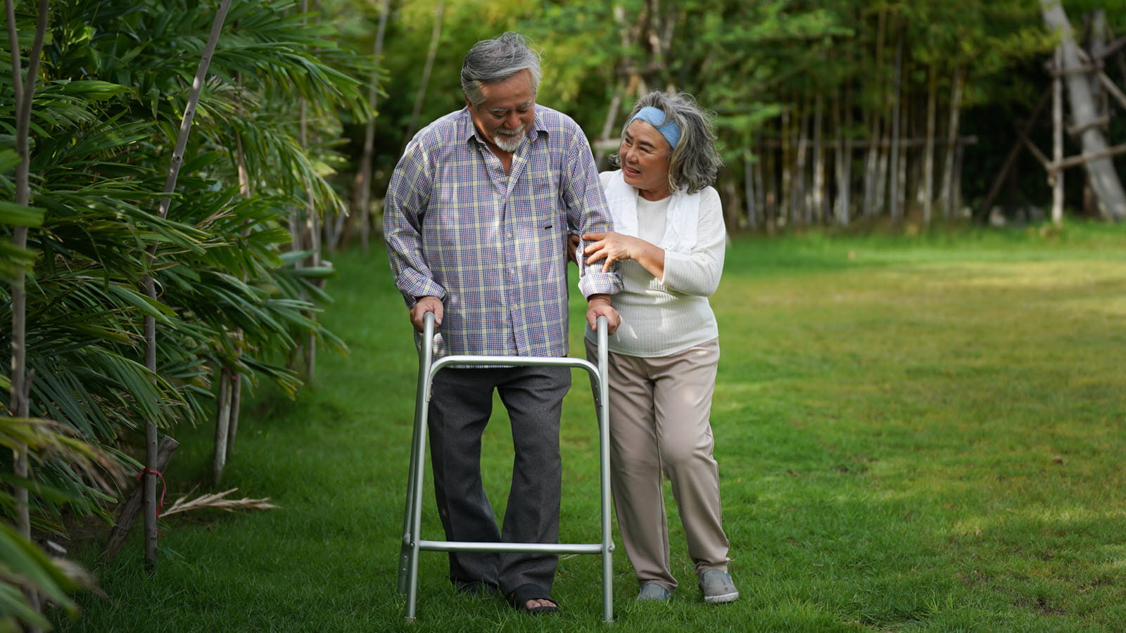 wife helps smiling husband with a walker in an outdoor setting