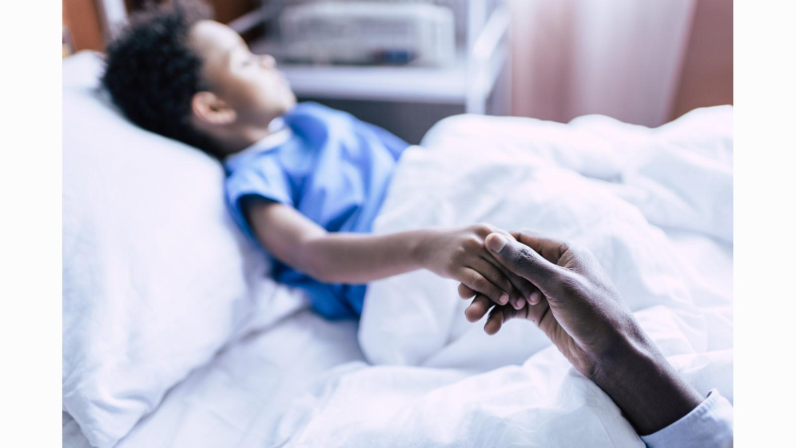 child in hospital bed with parent holding hand