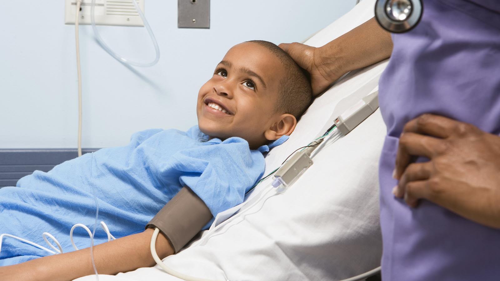 child in a hospital bed smiles at his nurse