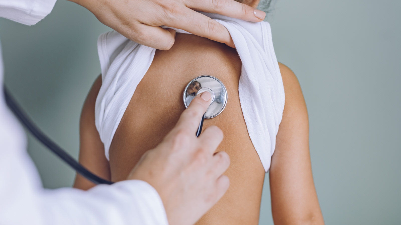 Doctor listens with a stethoscope pressed to the back of a young child.