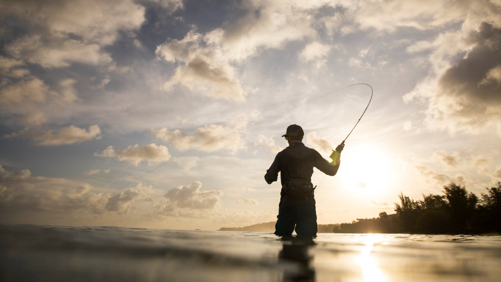 Silhouette of fly fisherman against a sunny sky