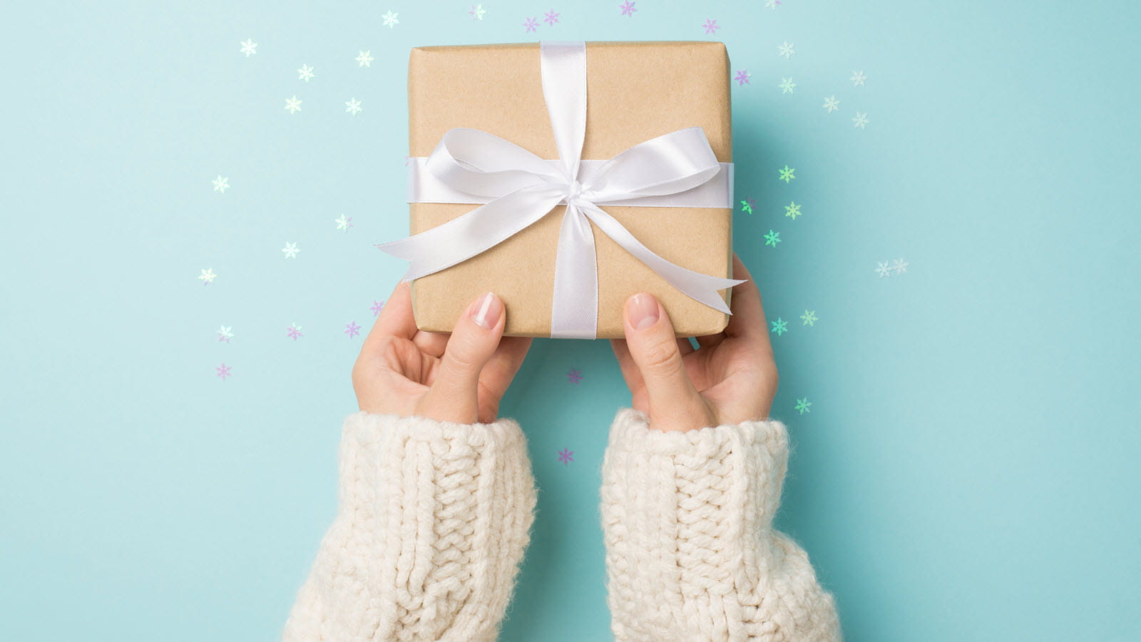 Sweatered arms reach out to give a present wrapped in a white bow against a blue starry background.