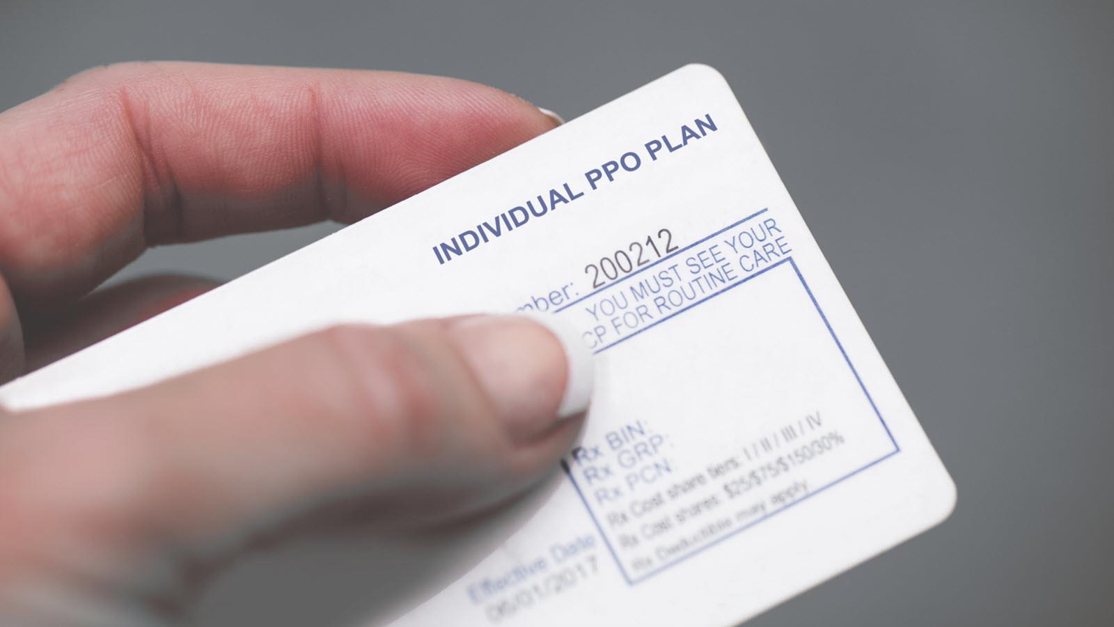 A hand holds an insurance card that says Individual PPO Plan