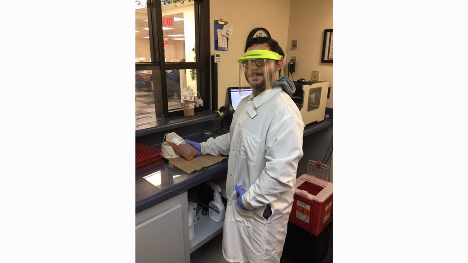 Isaiah Murillo wears a lab coat and face shield at CSL Plasma