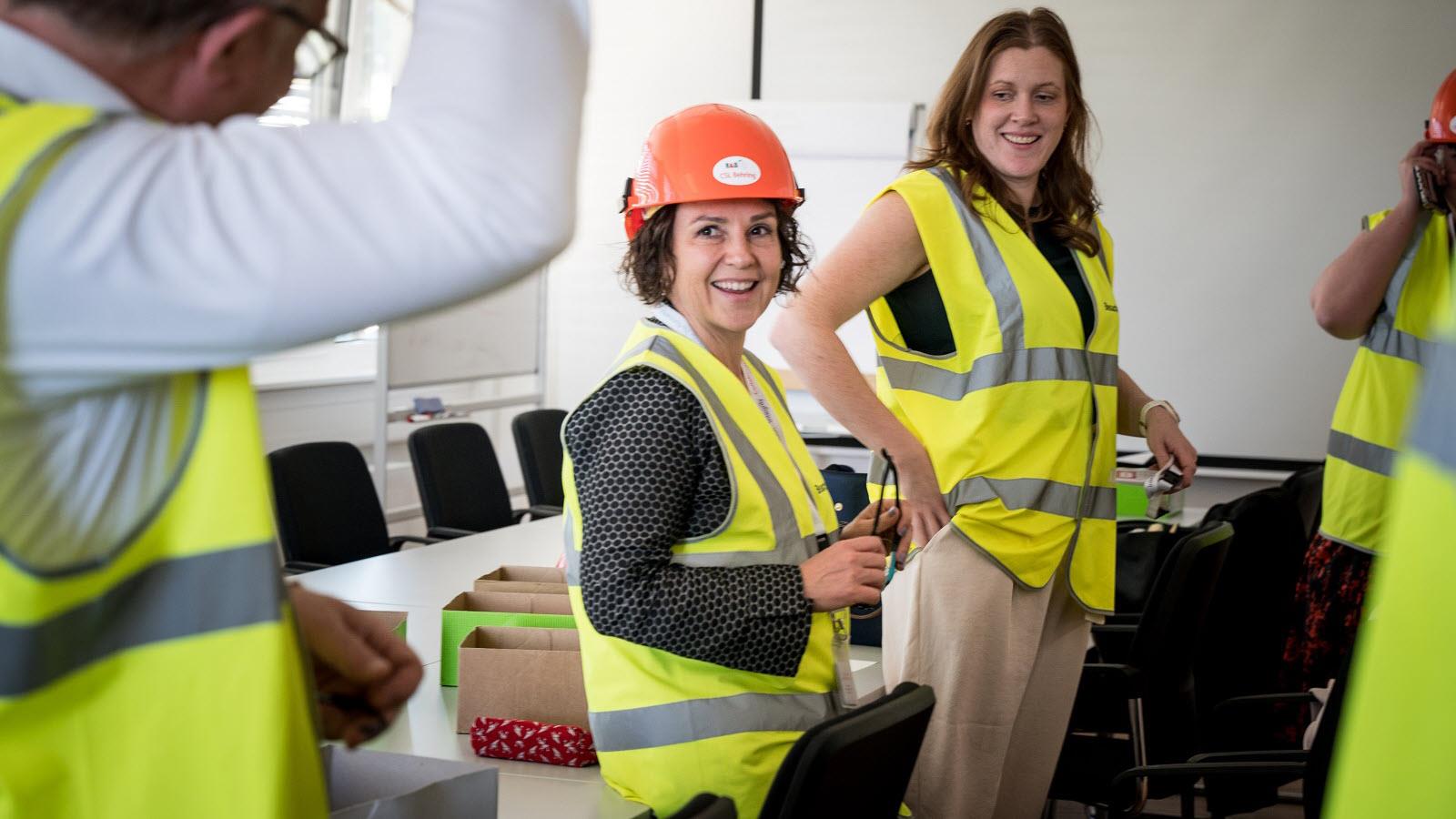 Jaala Pulford, in a yellow construction vest and orange hard hat, meets in a conference room with the team in Marburg, Germany.
