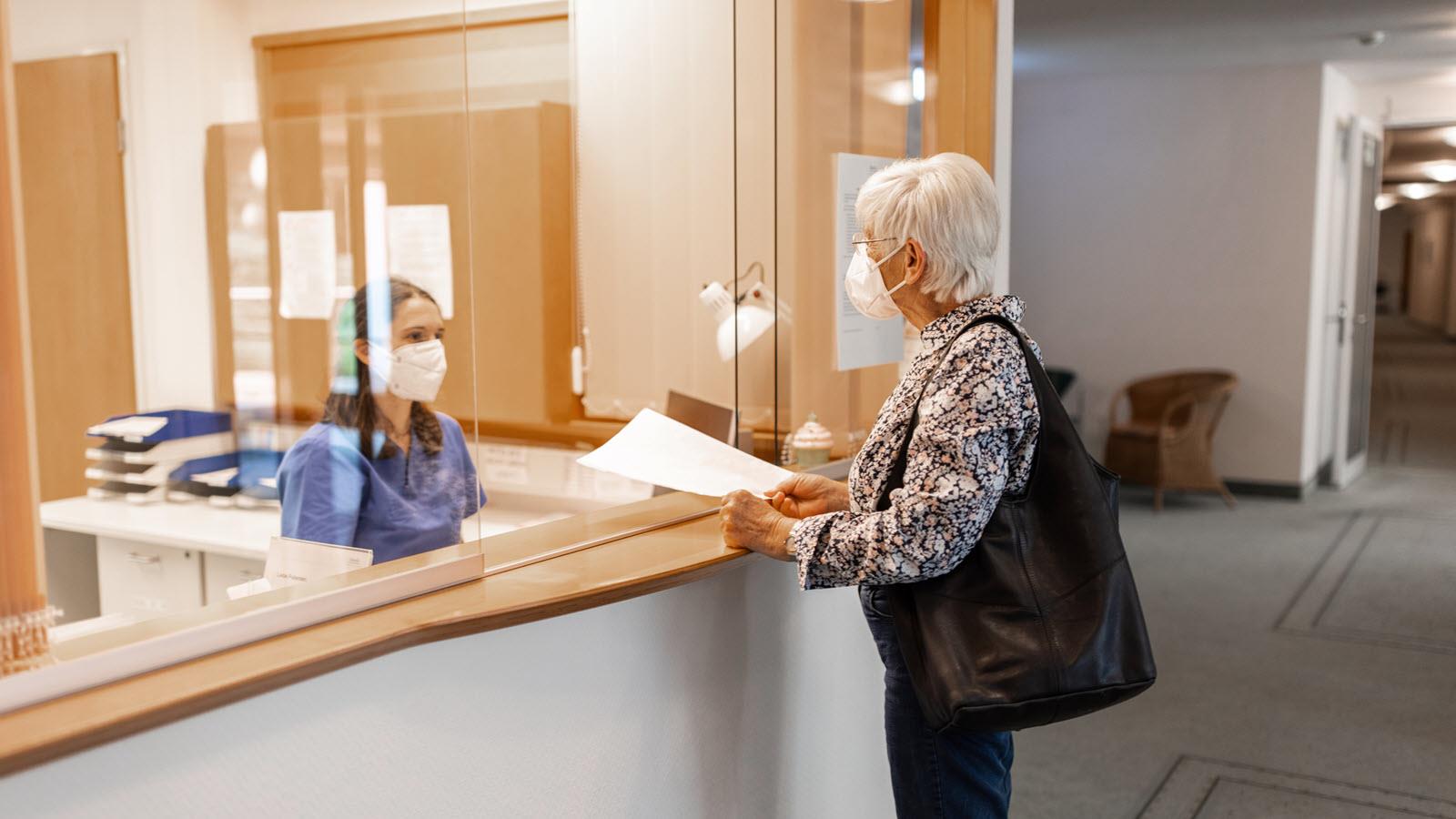 masked woman at a doctor appointment talking to the receptionist