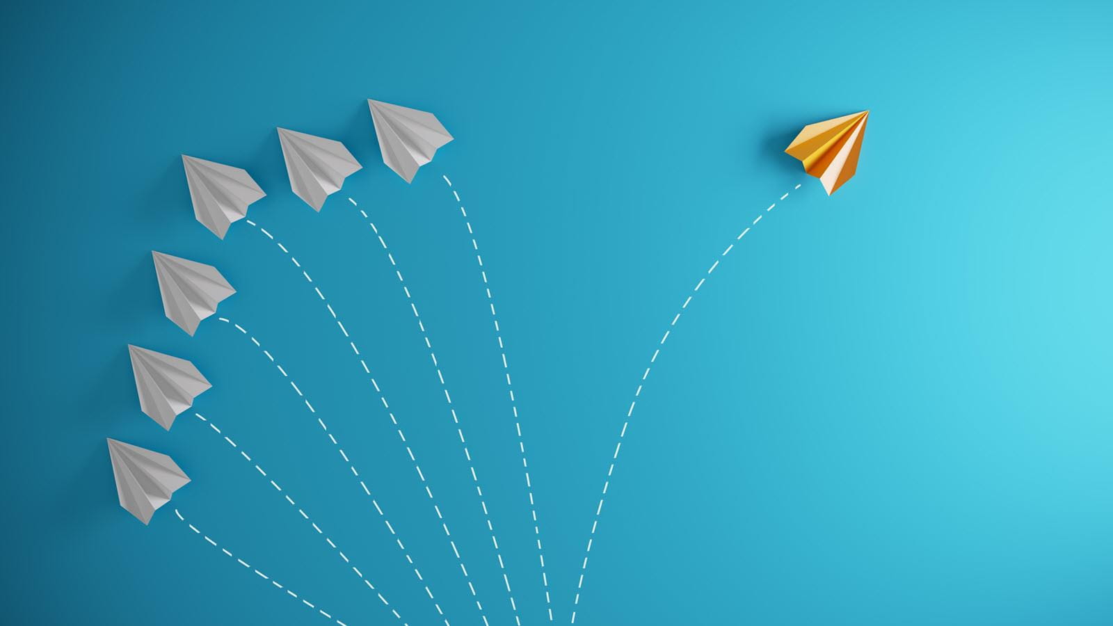 White paper airplanes on a blue background with one yellow plane flying in the opposite direction