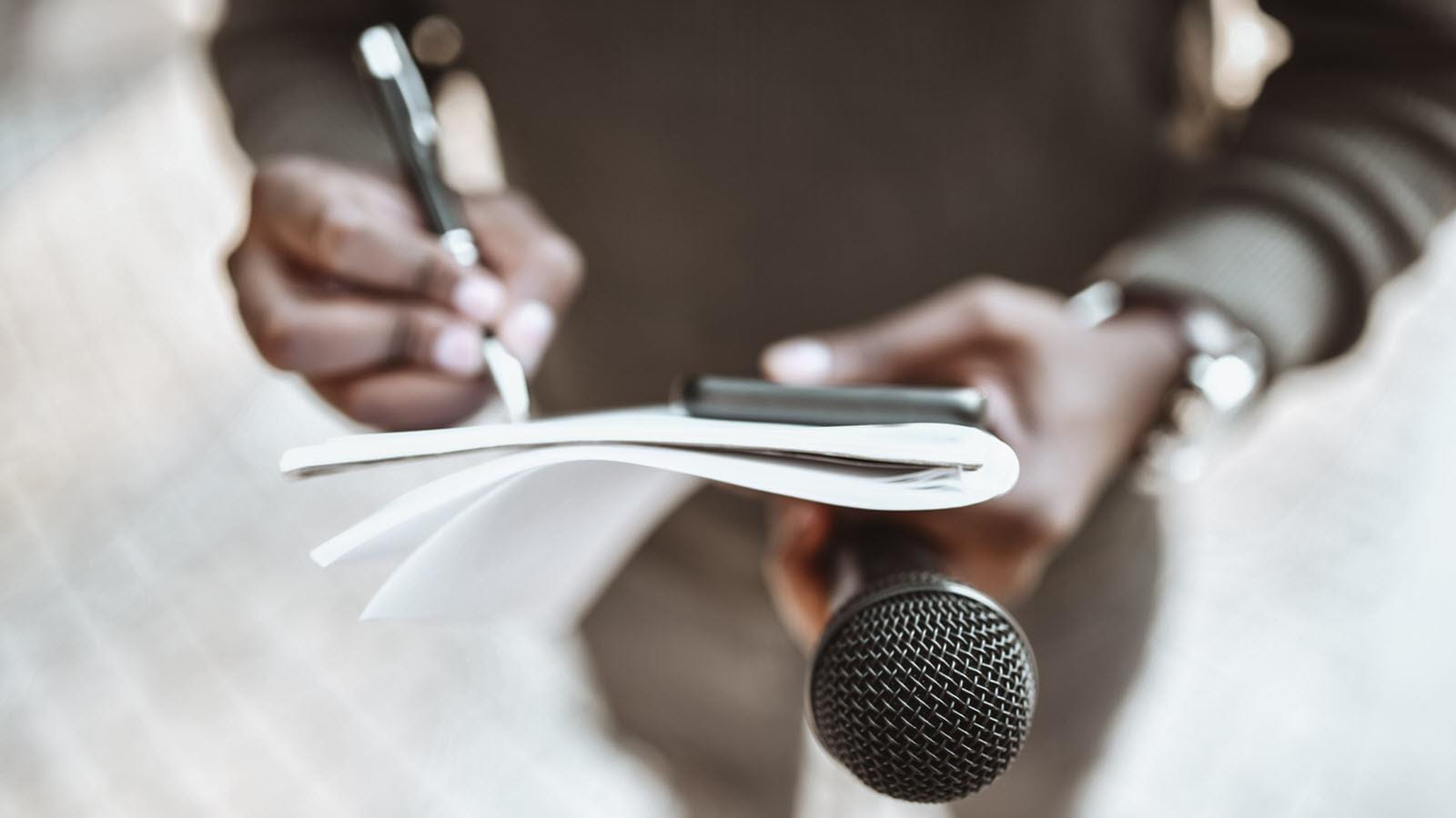 reporter holding a pen, notebook and microphone