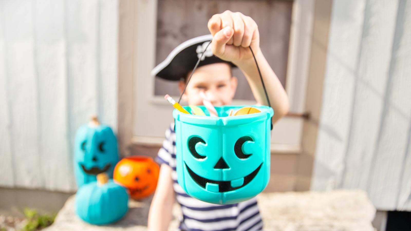 A child dressed as a pirate for Halloween holds a teal pumpkin bucket