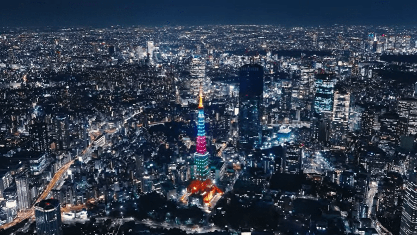 Aerial nighttime view of Tokyo, including the Tokyo Tower lit up in pink, blue and green colors for Rare Disease Day.