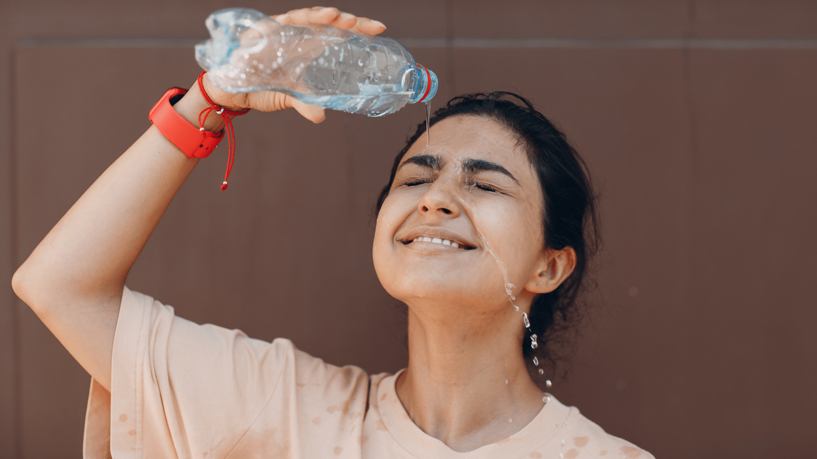 Young woman pours a bottle of water on her head.