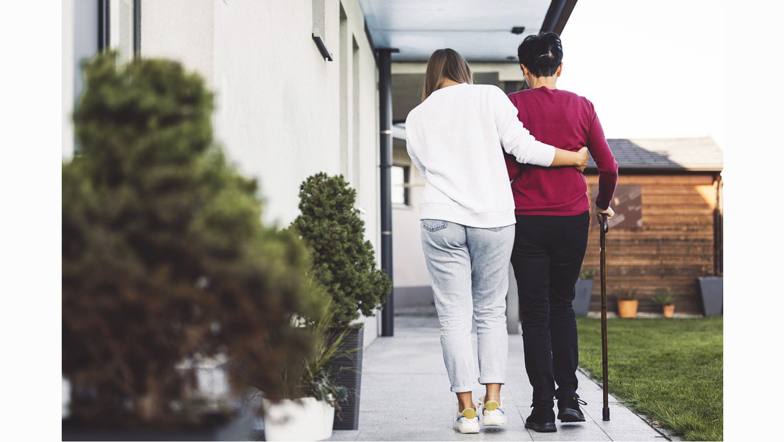 A caregiver helps a patient walk down a sidewalk.