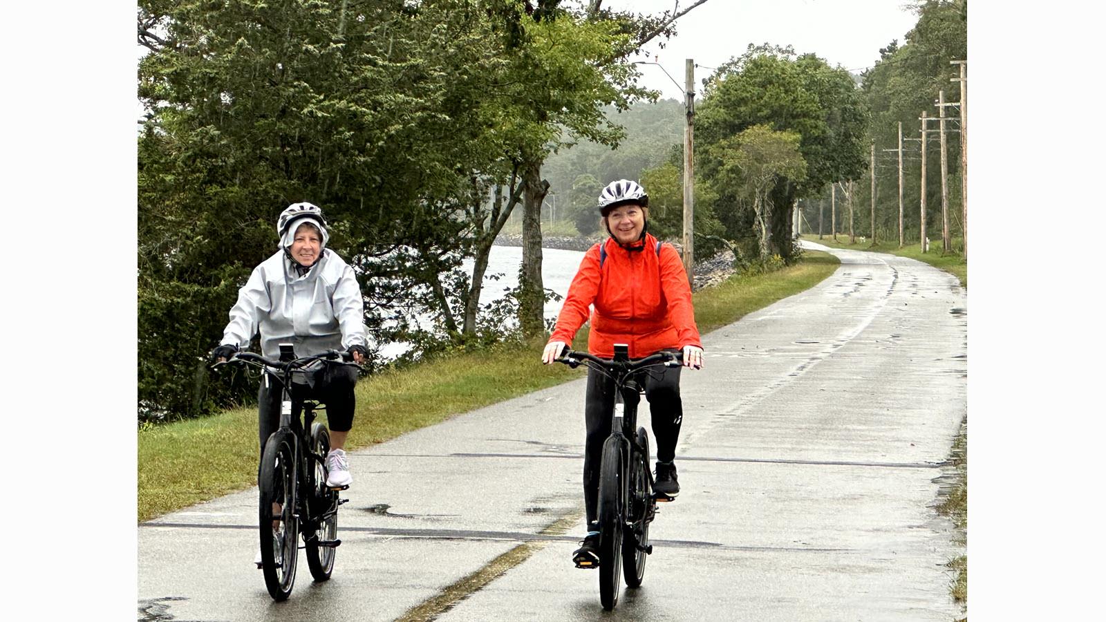 Two participants in the Escape to the Cape Bike Trek cycling on a wet road