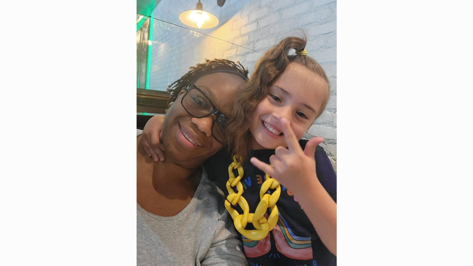 Exie and daughter Eden with a side ponytail showing the hand sign for "I love you."