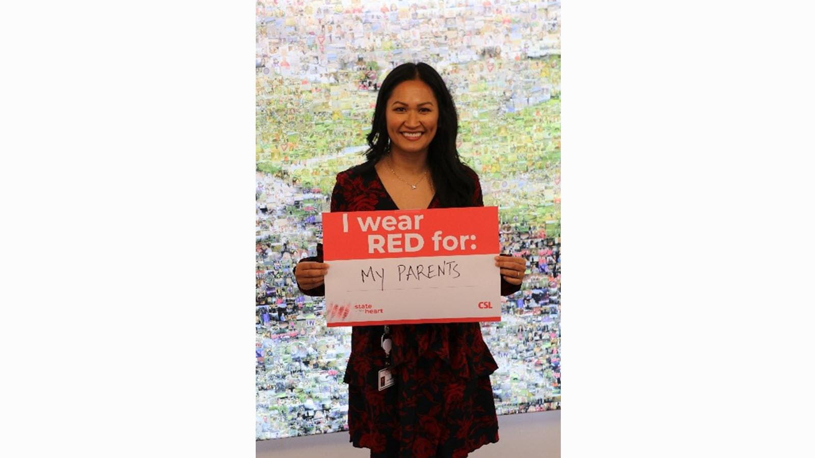 Jenny Mears, a leader on CSL's Cardiovascular team, holds a sign that says "I wear red for my parents."