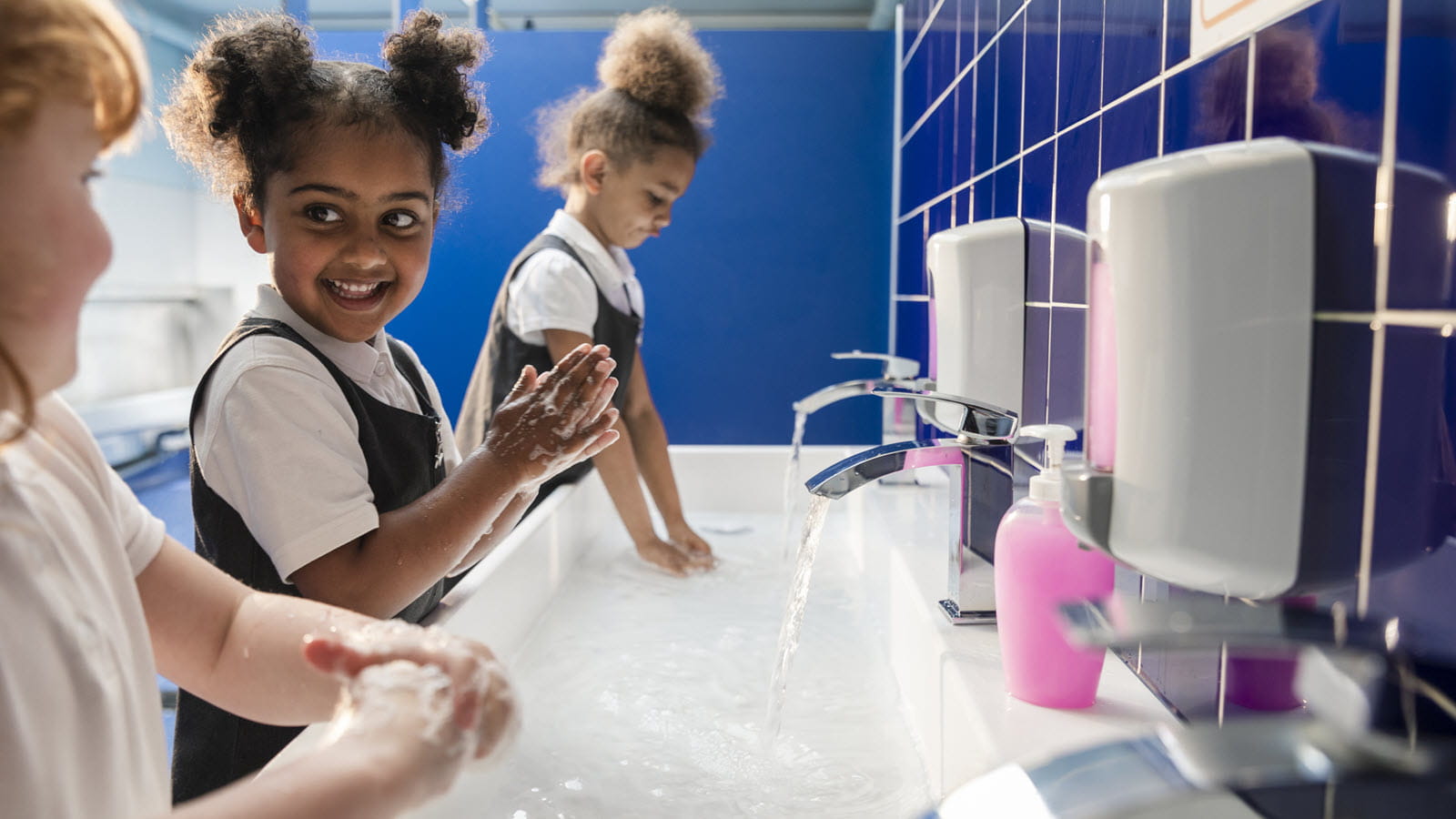 Three children wash up at a public restroom sink.
