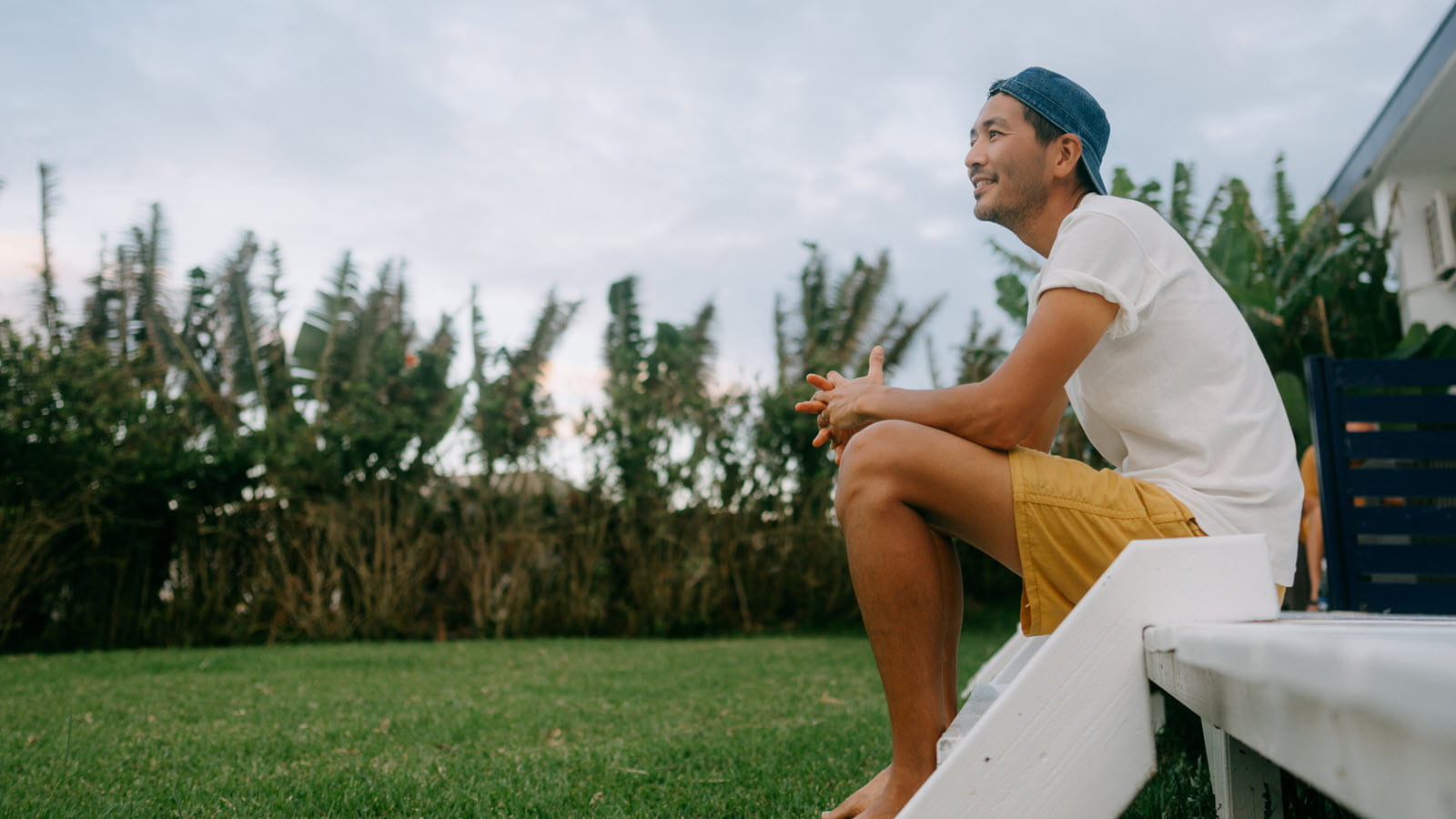Man in ball cap sits on back porch.