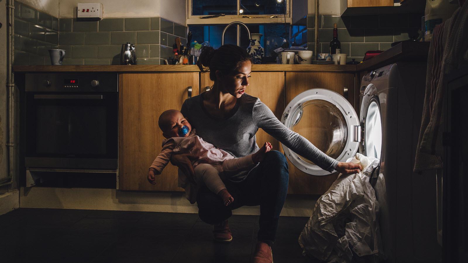 NIght scene of mom holding baby and putting laundry in the dryer