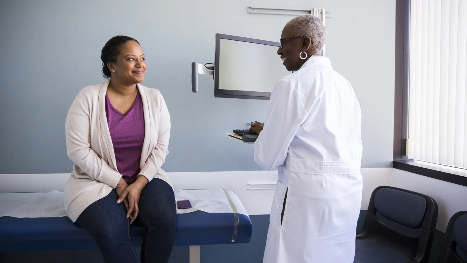 Patient in exam room smiles as she talks with the doctor.