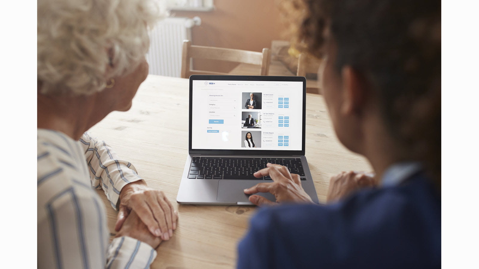 Two women review doctor options on a laptop screen.